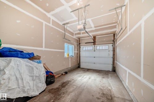 The property includes a spacious garage with a white overhead door featuring windows, a window providing natural light, and a concrete floor - 11 1530 Tamarack Boulevard, Edmonton, AB - Indoor Photo Showing Garage