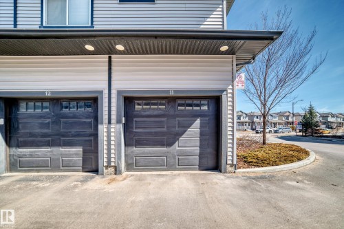 The property features two individual garages with panelled doors and upper window inserts, providing ample parking and storage - 11 1530 Tamarack Boulevard, Edmonton, AB - Outdoor