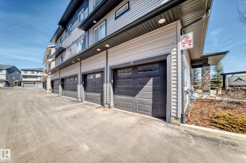 The property features a series of garages with dark sectional doors, set against light-colored siding - 11 1530 Tamarack Boulevard, Edmonton, AB - Outdoor