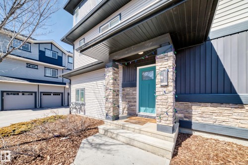 The property features a charming exterior with stone accents and a vibrant teal front door, complemented by a covered entrance - 11 1530 Tamarack Boulevard, Edmonton, AB - Outdoor