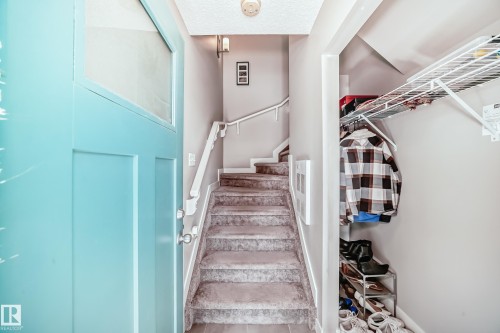 Entryway featuring a light blue door with a window, a carpeted staircase with white railings, and a closet area with wire shelving - 11 1530 Tamarack Boulevard, Edmonton, AB - Indoor