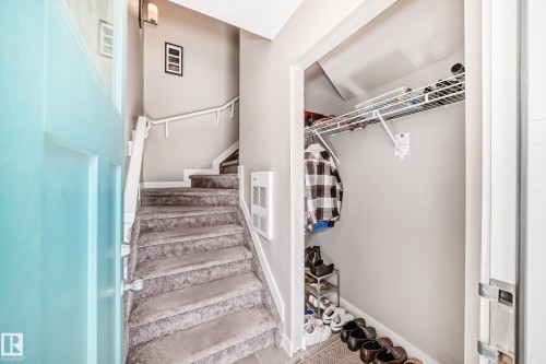 The property entrance features a light blue main door, carpeted stairs with a white handrail, and a built-in closet with wire shelving - 11 1530 Tamarack Boulevard, Edmonton, AB - Indoor