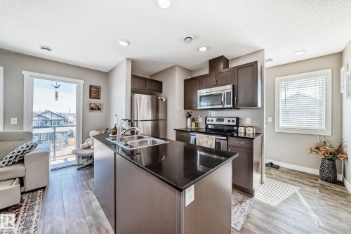 The property features a kitchen with dark cabinetry, stainless steel appliances, and a central island with a double sink - 11 1530 Tamarack Boulevard, Edmonton, AB - Indoor Photo Showing Kitchen With Double Sink With Upgraded Kitchen