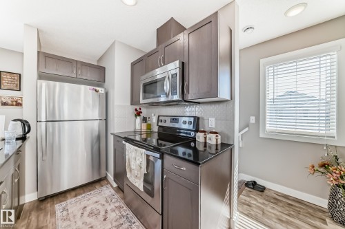 The kitchen features stainless steel appliances, including a microwave, oven, and refrigerator - 11 1530 Tamarack Boulevard, Edmonton, AB - Indoor Photo Showing Kitchen With Upgraded Kitchen