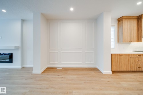 This property features light-toned flooring throughout, a modern electric fireplace with a white mantel, and contemporary wall paneling - 9536 148 Street, Edmonton, AB - Indoor