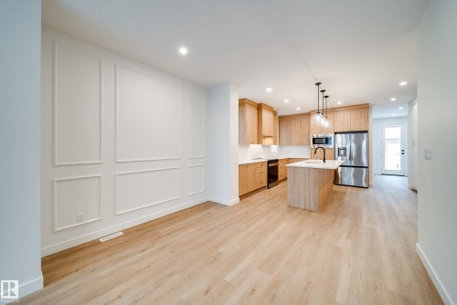 Open concept living space featuring light-toned flooring, a kitchen with wooden cabinetry, stainless steel appliances, and a central island with an integrated sink - 9536 148 Street, Edmonton, AB - Indoor Photo Showing Kitchen
