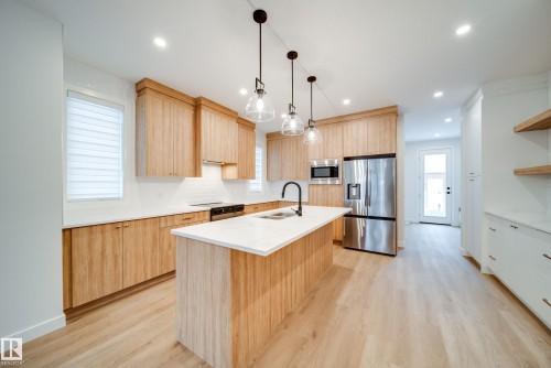 The kitchen features light wood cabinetry, a central island with a white countertop, and stainless steel appliances - 9536 148 Street, Edmonton, AB - Indoor Photo Showing Kitchen With Double Sink With Upgraded Kitchen