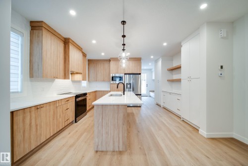 Kitchen featuring light wood cabinetry, white countertops, stainless steel appliances, and a central island with a sink and modern pendant lighting - 9536 148 Street, Edmonton, AB - Indoor Photo Showing Kitchen With Upgraded Kitchen