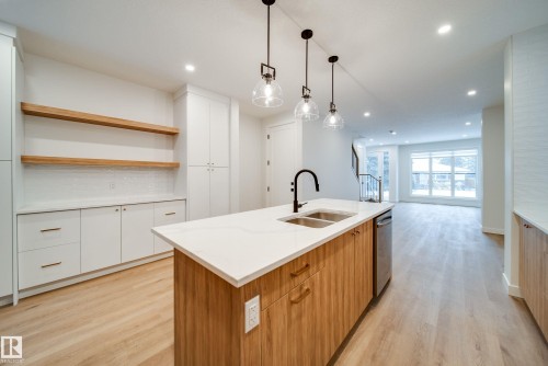 The kitchen features a large island with a double sink and a modern black faucet, white countertops, and wood-paneled cabinetry - 9536 148 Street, Edmonton, AB - Indoor Photo Showing Kitchen With Double Sink
