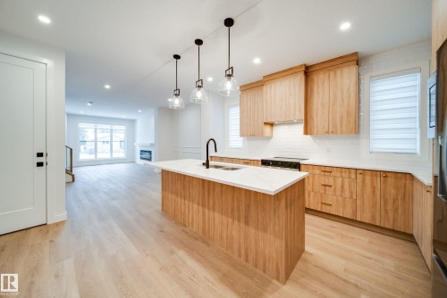 The kitchen features wood cabinetry, a white countertop island with a sink, and pendant lighting - 9536 148 Street, Edmonton, AB - Indoor Photo Showing Kitchen With Double Sink With Upgraded Kitchen
