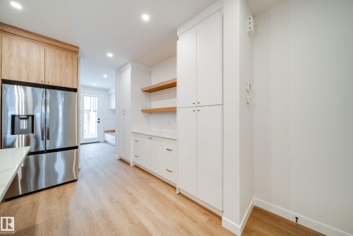 Modern kitchen featuring light wood flooring, white cabinetry with gold hardware, and a stainless steel refrigerator - 9536 148 Street, Edmonton, AB - Indoor