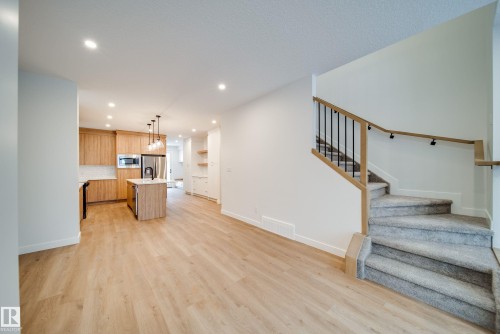 The property features an open-concept living space with light wood-tone flooring, a modern kitchen with a center island and stainless steel appliances, and a carpeted staircase with a contemporary wood and metal railing - 9536 148 Street, Edmonton, AB - Indoor