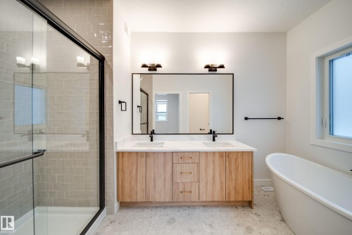 Bathroom featuring a double vanity with light wood cabinetry and gold hardware, a large rectangular mirror, and an adjacent freestanding bathtub - 9536 148 Street, Edmonton, AB - Indoor Photo Showing Bathroom