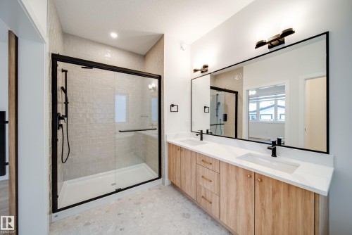 The bathroom features a spacious shower with a clear glass enclosure and black trim, a double vanity with light wood cabinetry, white countertops, and dual rectangular sinks with black fixtures, and a large mirror with black framing - 9536 148 Street, Edmonton, AB - Indoor