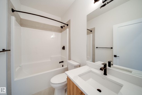 Bathroom featuring a white bathtub and shower combination with a curved shower rod, a toilet, and a vanity with a white countertop and rectangular sink - 9536 148 Street, Edmonton, AB - Indoor Photo Showing Bathroom