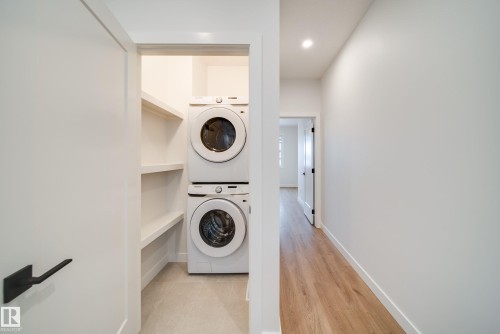 Laundry area featuring a stacked washer and dryer, with built-in shelving, and light wood flooring - 9536 148 Street, Edmonton, AB - Indoor Photo Showing Laundry Room