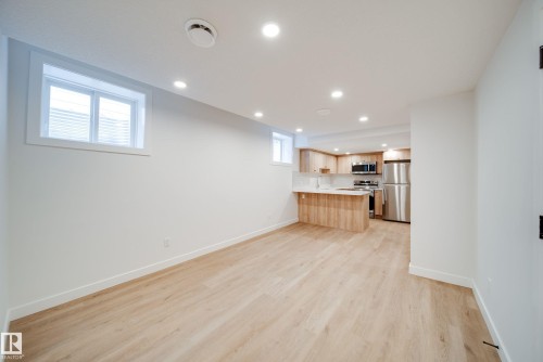 Spacious open-plan area featuring light-colored flooring, recessed lighting, and a kitchen area with light wood cabinetry, stainless steel appliances, and a breakfast bar - 9536 148 Street, Edmonton, AB - Indoor