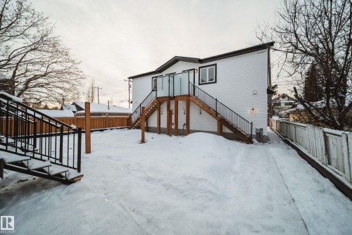 The property features a white exterior with black trim, a wood deck with glass panel railings, and two exterior staircases with black metal railings - 9536 148 Street, Edmonton, AB - Outdoor