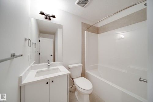 This bathroom features a white vanity with a rectangular sink, a mirror, and a modern light fixture - 9536 148 Street, Edmonton, AB - Indoor Photo Showing Bathroom