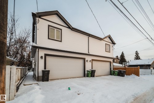 The property features a two-story structure with white siding and dark trim, including two garage doors and upper-level windows - 9536 148 Street, Edmonton, AB - Outdoor