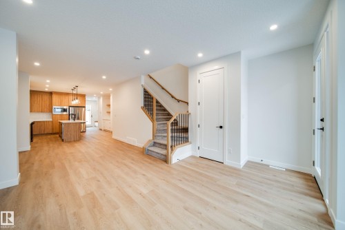 The open concept living area features light-toned flooring, a staircase with a carpeted runner and dark metal balusters, and a kitchen with wooden cabinetry, a central island, and stainless steel appliances - 9536 148 Street, Edmonton, AB - Indoor