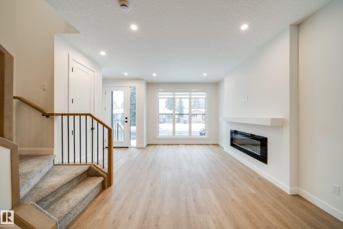The property features light-colored flooring throughout the main living area, a modern electric fireplace with a white mantel, and a large window providing ample natural light - 9536 148 Street, Edmonton, AB - Indoor With Fireplace