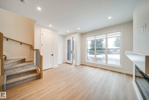 This bright living area features light-toned flooring, a carpeted staircase with wood and metal railings, and a large window providing views of the outdoors - 9536 148 Street, Edmonton, AB - Indoor Photo Showing Other Room