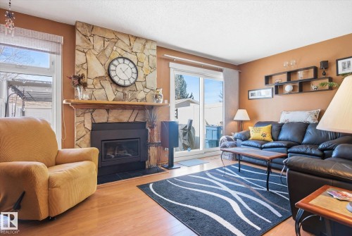 Living area featuring a stone fireplace with a wooden mantel, a sliding glass door, and hardwood flooring - 3237 142 Avenue, Edmonton, AB - Indoor Photo Showing Living Room With Fireplace