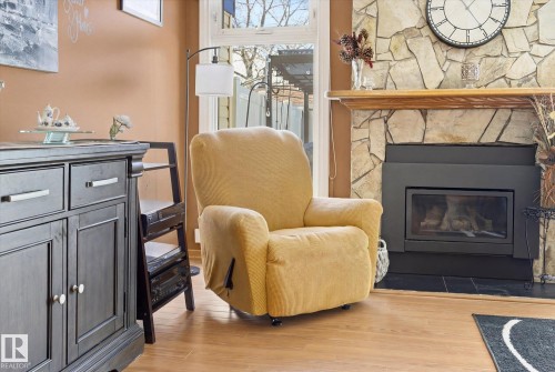 Living area featuring a stone fireplace with a wooden mantel, hardwood flooring, and a large window providing outdoor views - 3237 142 Avenue, Edmonton, AB - Indoor Photo Showing Living Room With Fireplace