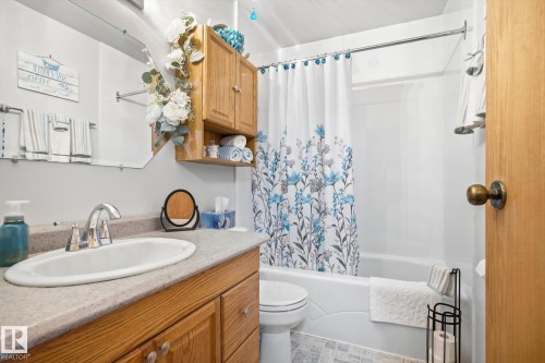 Bathroom featuring a vanity with a light wood base cabinet, a white sink, and a shower with a white tub - 3237 142 Avenue, Edmonton, AB - Indoor Photo Showing Bathroom