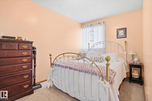 This room offers a comfortable atmosphere with soft peach-colored walls and a carpeted floor - 3237 142 Avenue, Edmonton, AB - Indoor Photo Showing Bedroom