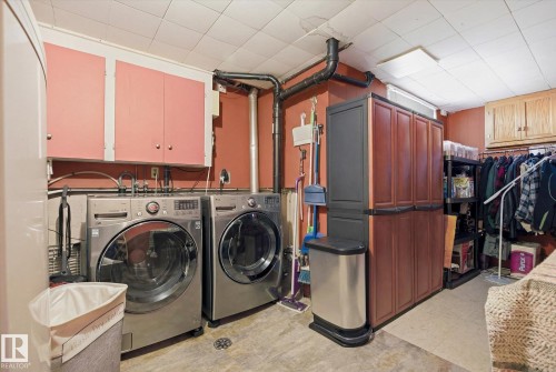 Functional utility area with a drop ceiling, featuring a front-loading washing machine and dryer, along with wall-mounted cabinetry - 3237 142 Avenue, Edmonton, AB - Indoor Photo Showing Laundry Room