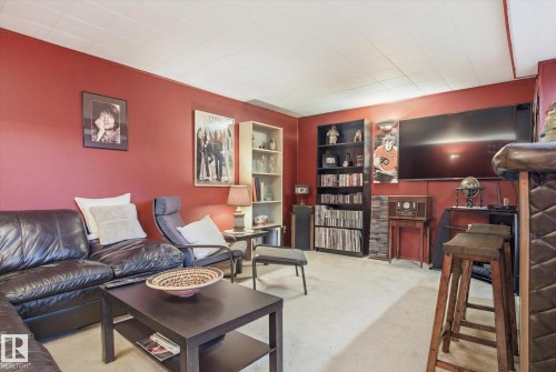 The property offers a living area with a large wall-mounted television, red walls, and light-colored carpeting - 3237 142 Avenue, Edmonton, AB - Indoor
