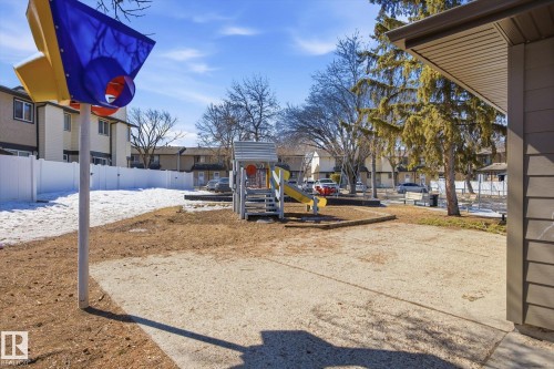 This property features a community playground with a slide and climbing structure, set on a sand base - 3237 142 Avenue, Edmonton, AB - Outdoor