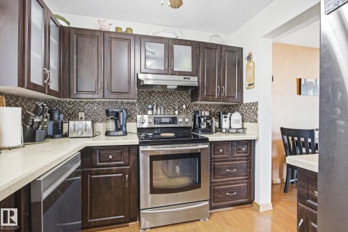 Kitchen featuring dark wood cabinetry, a mosaic tile backsplash, light countertops, and stainless steel appliances including a range, dishwasher, and refrigerator - 3237 142 Avenue, Edmonton, AB - Indoor Photo Showing Kitchen
