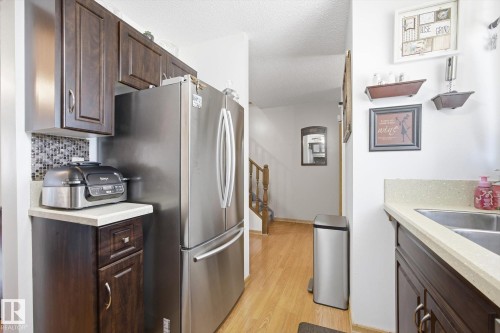 The kitchen features dark wood cabinetry, a stainless steel refrigerator, and light-colored countertops - 3237 142 Avenue, Edmonton, AB - Indoor Photo Showing Kitchen With Stainless Steel Kitchen With Double Sink