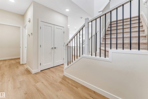 This welcoming entryway features light wood flooring, white trim, and a carpeted staircase with dark metal balusters - 91 Dansereau Way, Beaumont, AB - Indoor Photo Showing Other Room
