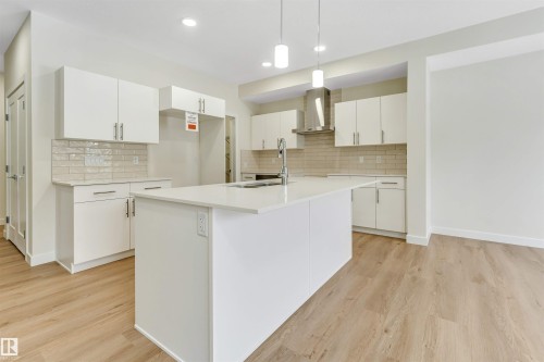 Modern kitchen featuring white cabinetry, light-colored countertops, a tile backsplash, and light wood flooring - 91 Dansereau Way, Beaumont, AB - Indoor Photo Showing Kitchen With Upgraded Kitchen