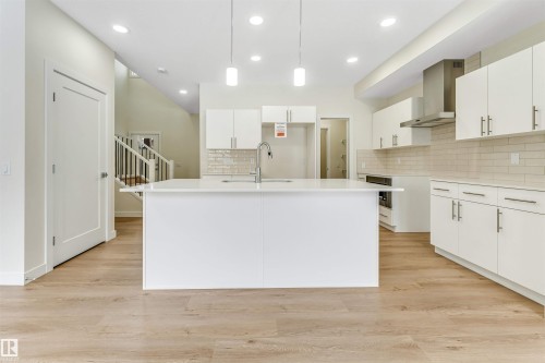 The kitchen features a large island with a sink and pendant lighting, white cabinetry, and light-colored subway tile backsplash - 91 Dansereau Way, Beaumont, AB - Indoor Photo Showing Kitchen With Upgraded Kitchen
