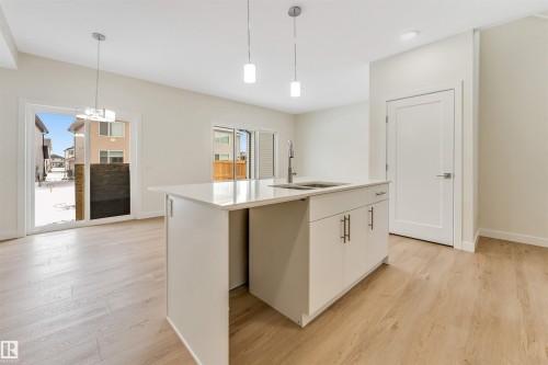 The kitchen features a central island with a sink and modern pendant lighting, complemented by light-colored flooring - 91 Dansereau Way, Beaumont, AB - Indoor Photo Showing Kitchen With Double Sink