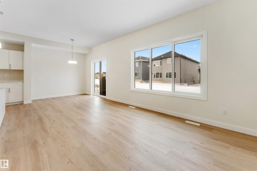 This expansive room features light-toned flooring, white walls, and a large window providing views of the exterior - 91 Dansereau Way, Beaumont, AB - Indoor
