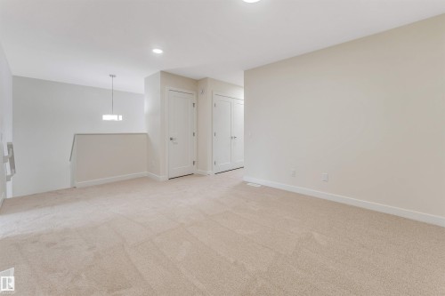This spacious carpeted area features neutral-toned walls, recessed lighting, and a contemporary pendant light fixture - 91 Dansereau Way, Beaumont, AB - Indoor Photo Showing Other Room