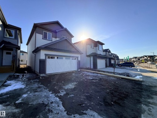 This property features a two-story design with a prominent white garage door and dark gray trim accents - 91 Dansereau Way, Beaumont, AB - Outdoor
