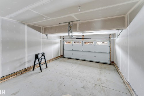 The garage features a concrete floor, white walls, and a white overhead garage door with windows - 91 Dansereau Way, Beaumont, AB - Indoor Photo Showing Garage