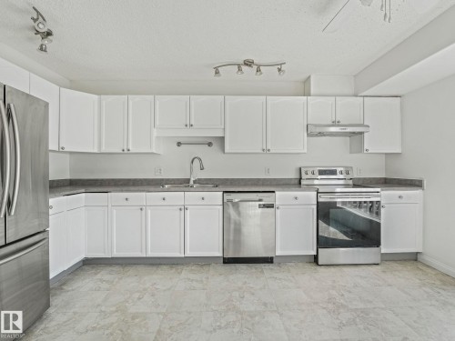 The kitchen features extensive white cabinetry, stainless steel appliances, a corner sink with a gooseneck faucet, and track lighting - 675 Mcallister Loop, Edmonton, AB - Indoor Photo Showing Kitchen