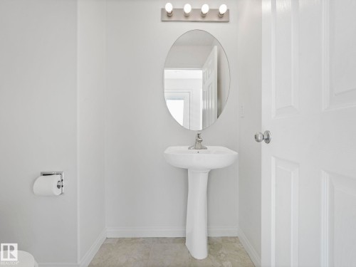 The bathroom features a pedestal sink with a chrome faucet, an oval mirror, and a four-bulb vanity light fixture - 675 Mcallister Loop, Edmonton, AB - Indoor Photo Showing Other Room