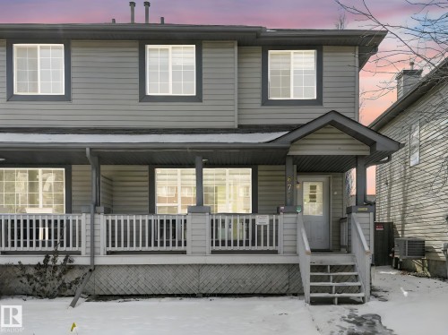 The property features a two-story exterior with grey siding and white-framed windows, complemented by a covered porch with white railings - 675 Mcallister Loop, Edmonton, AB - Outdoor With Deck Patio Veranda
