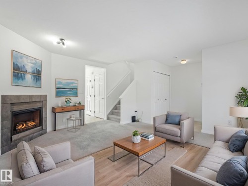 This living space features a fireplace with a stone surround, light-colored walls, and a combination of carpet and wood flooring - 675 Mcallister Loop, Edmonton, AB - Indoor Photo Showing Living Room With Fireplace