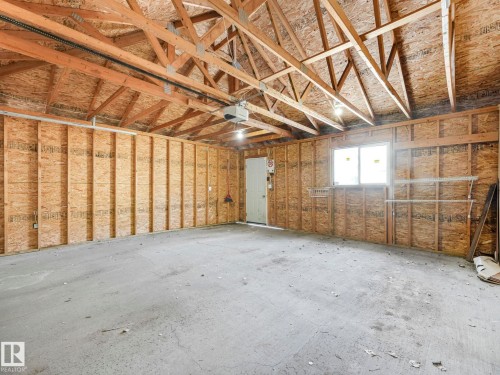 The property includes an expansive garage space with a concrete floor, exposed wooden rafters, and a window for natural light - 675 Mcallister Loop, Edmonton, AB - Indoor