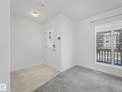 Entryway and living space featuring a white door with glass panels, light-colored tile flooring, and grey carpeting - 675 Mcallister Loop, Edmonton, AB - Indoor Photo Showing Other Room
